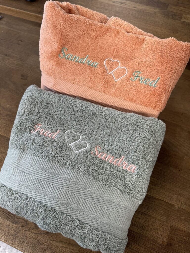 Deux serviettes de bain brodées aux prénoms Sandra et Fred reliés par deux cœurs