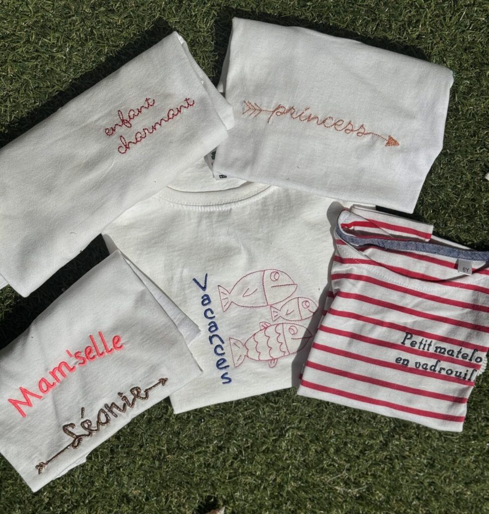 T-shirts enfants et marinière brodés de prénoms et de messages, posés sur l'herbe