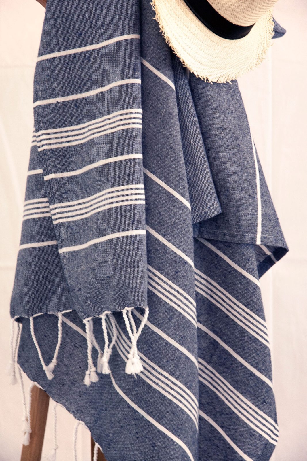 Fouta bleu marine à rayures blanches et à franges nouées, suspendue à une échelle en bois sous un chapeau de paille